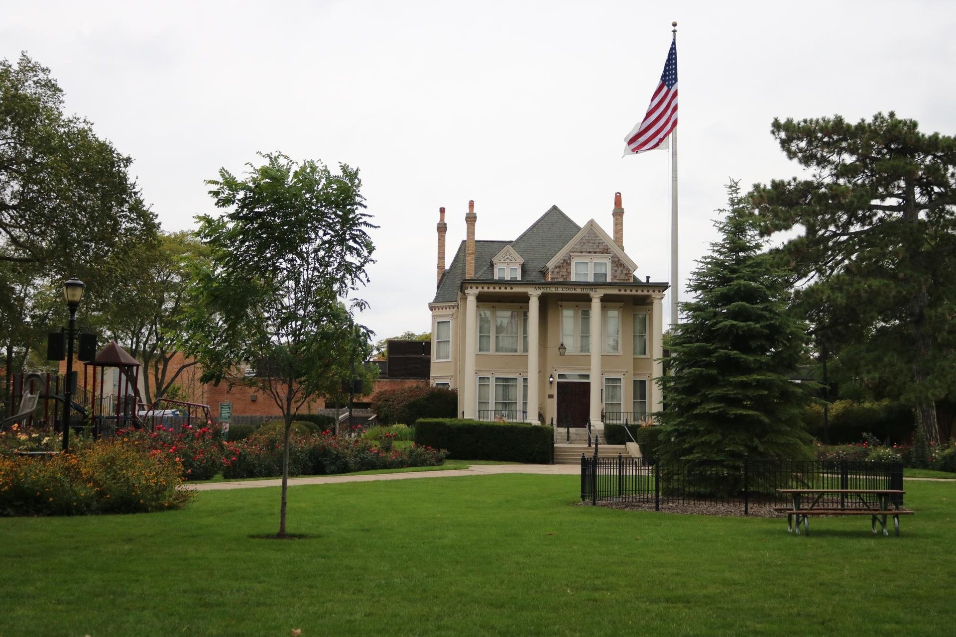 Victorian mansion with American flag in front yard surrounded by green lawn and trees