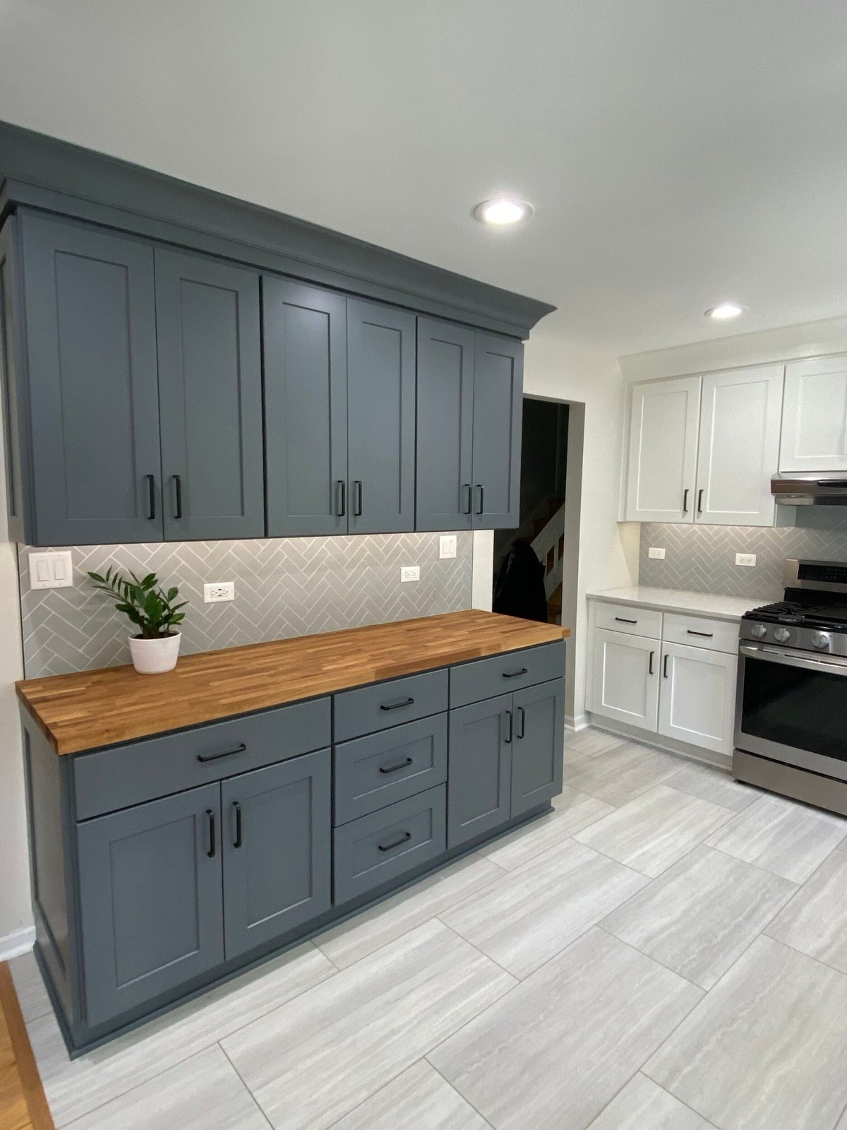 Modern kitchen with blue-gray cabinetry, wooden countertop island, herringbone tile backsplash, white appliances, and gray tile flooring