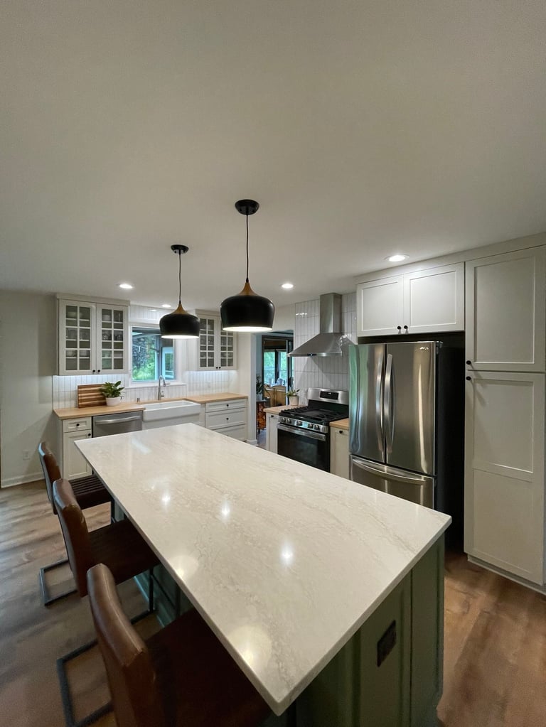 Modern kitchen with white quartz island, black pendant lights, stainless steel appliances, and sage green cabinetry