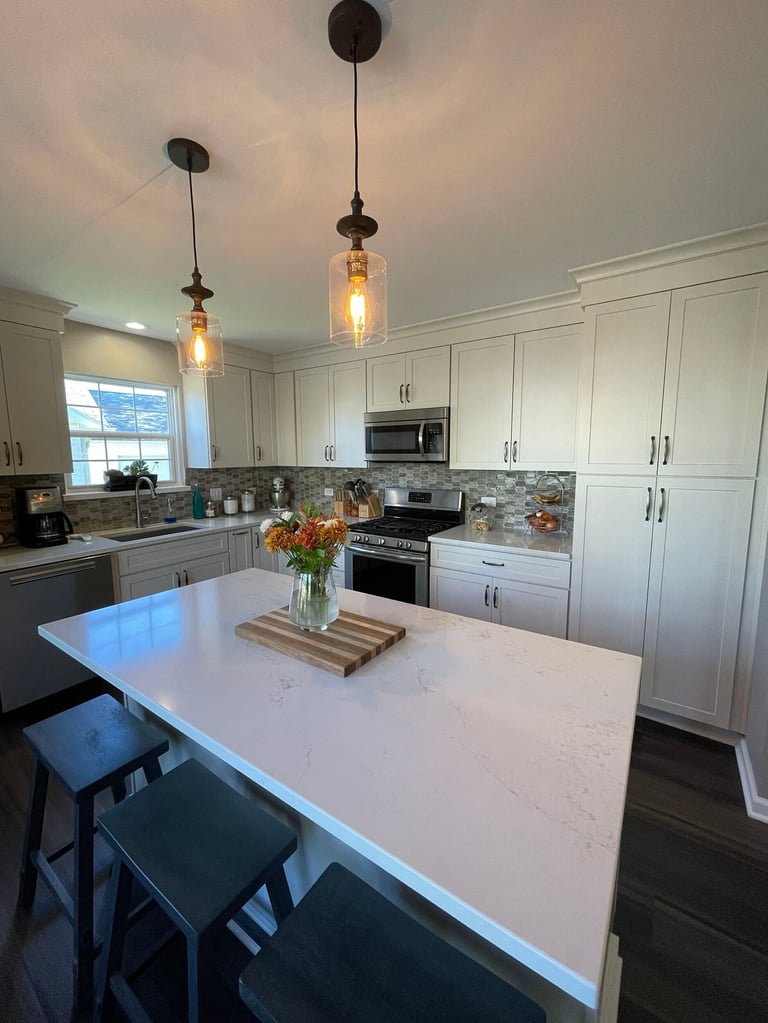 Modern kitchen with white cabinetry, white marble island, pendant lights, and black bar stools with a flower arrangement