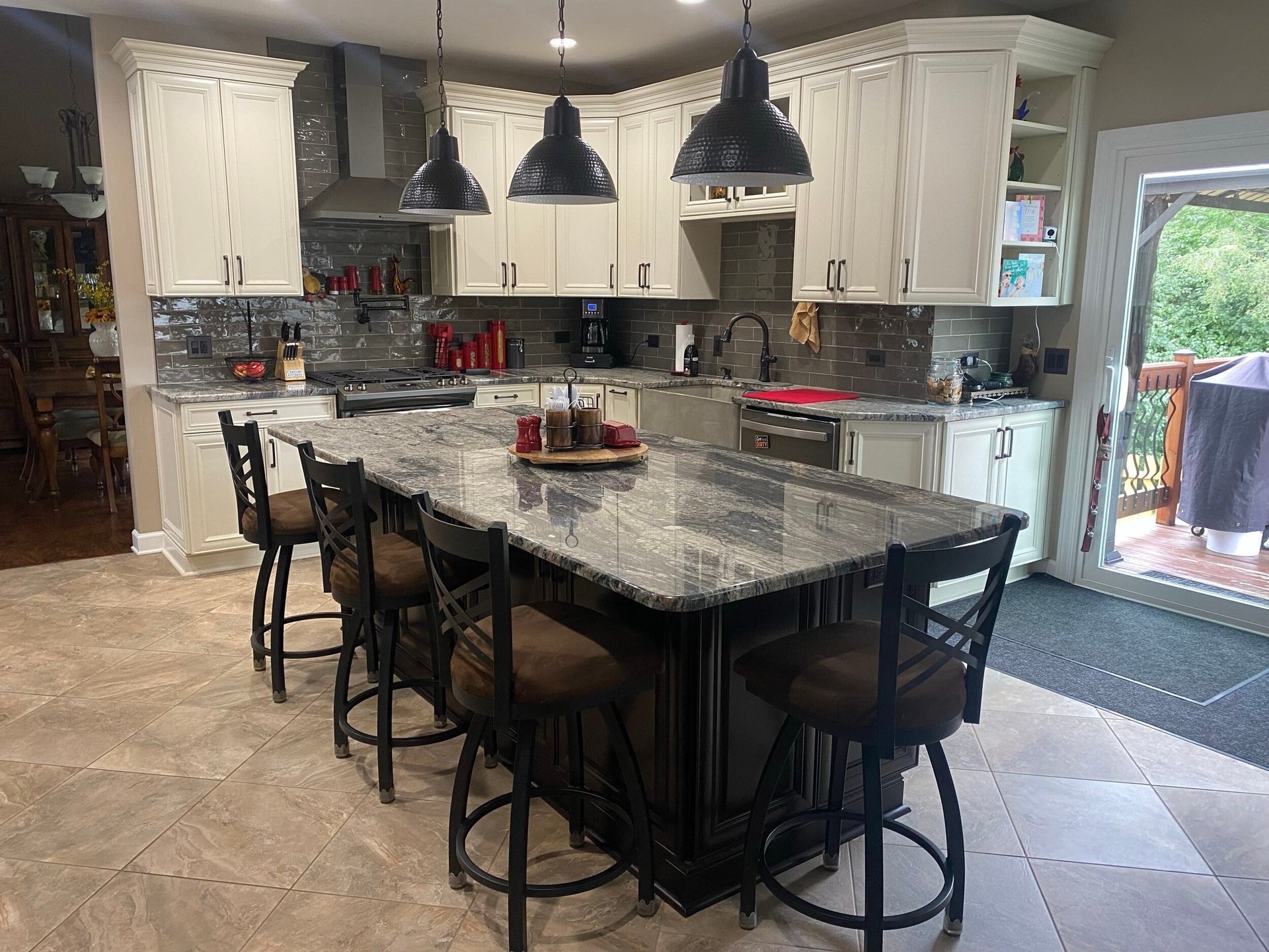 Modern kitchen with white cabinetry, black island, marble countertops, pendant lights, and bar seating for four