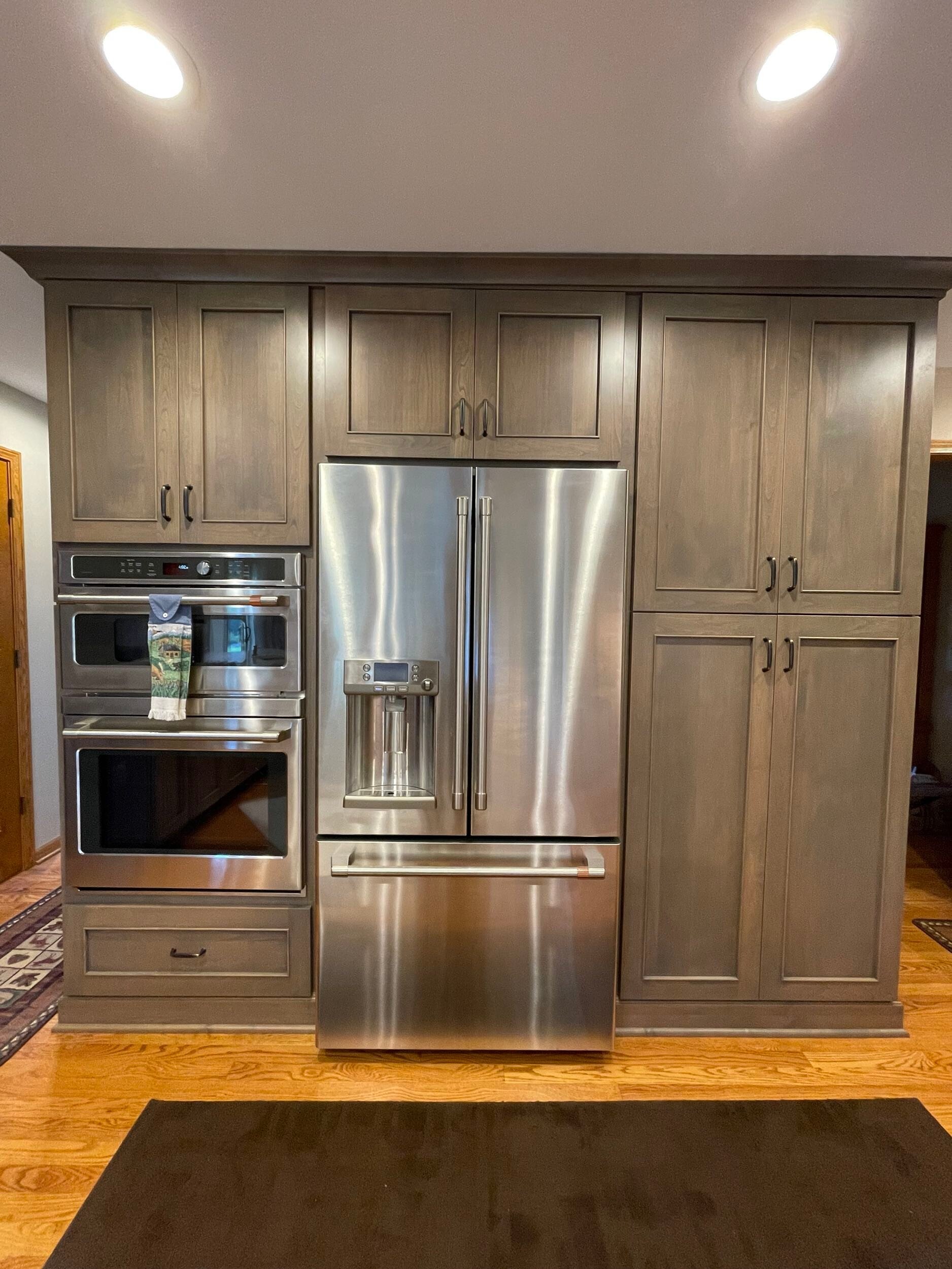 Modern kitchen with gray cabinetry, stainless steel appliances, and wooden flooring under recessed lighting