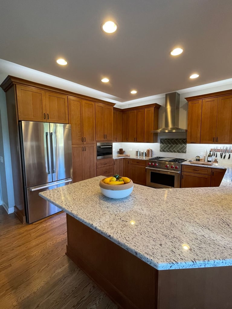 Modern kitchen with wood cabinets, granite island countertop, stainless steel refrigerator, and recessed ceiling lights