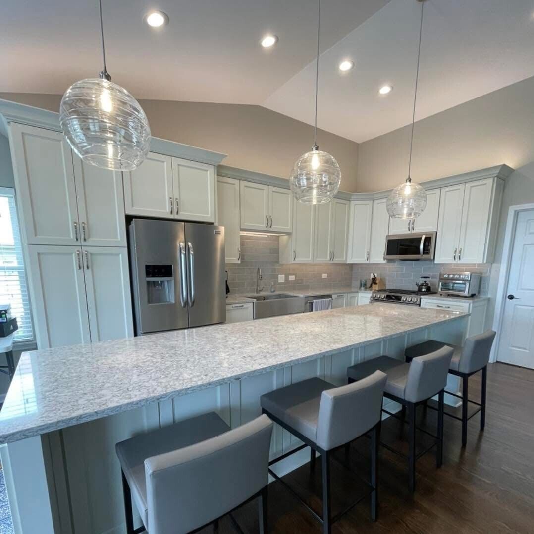 Modern kitchen with white cabinetry, gray island, pendant lights, stainless steel appliances, and granite countertops