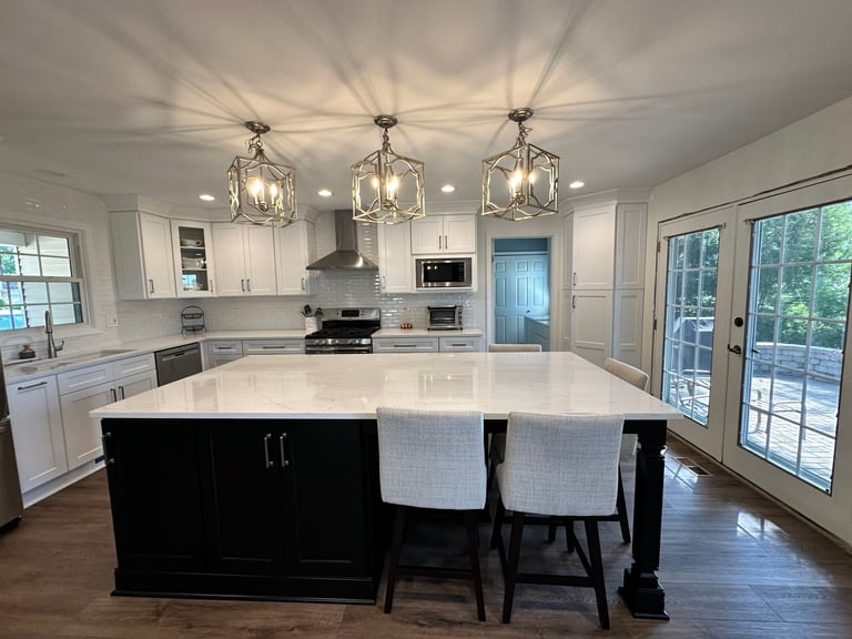 Modern kitchen with white cabinetry, large black island with seating, three pendant lights, and glass doors overlooking trees