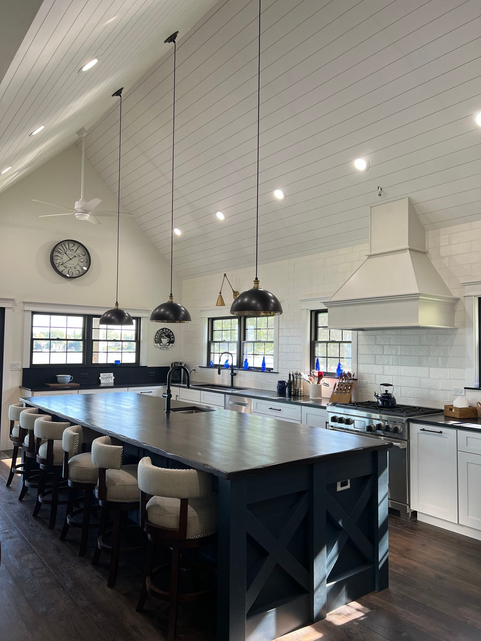Modern kitchen with large black island, pendant lights, white subway tile backsplash, and shiplap ceiling