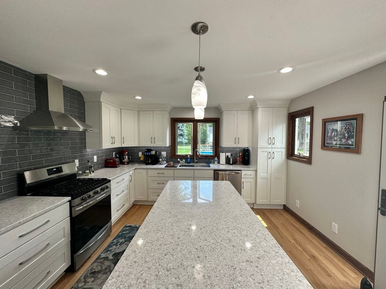 Modern kitchen with white cabinetry, gray subway tile backsplash, stainless steel appliances, and granite countertop island with pendant lighting