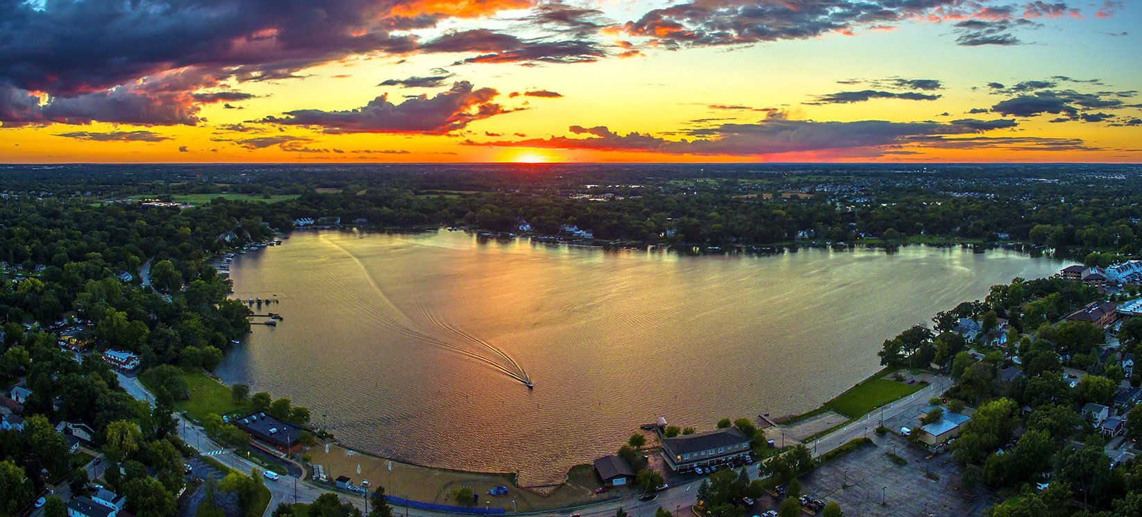 Aerial view of a lake surrounded by trees and houses at sunset with colorful sky
