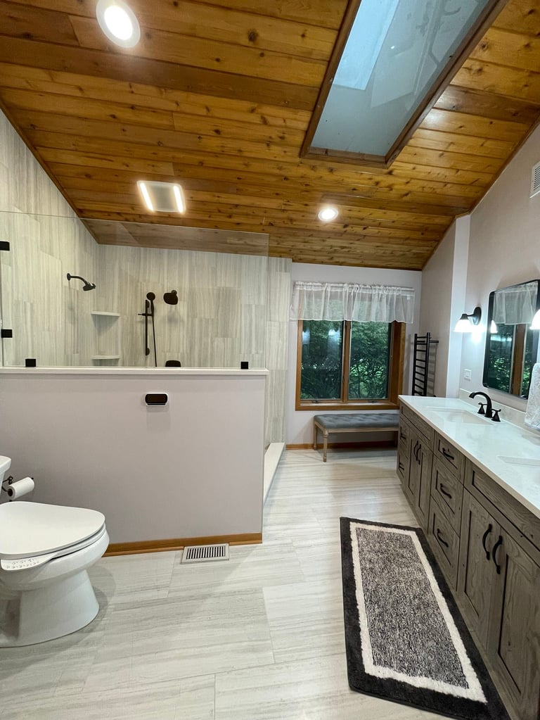 Modern bathroom with wooden ceiling, light tile flooring, white toilet, glass shower enclosure, and dual vanity sink with mirror