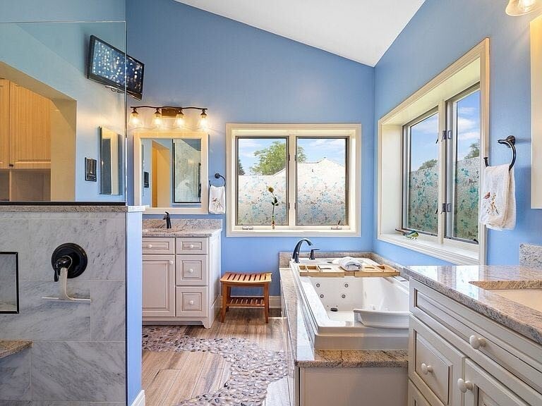Modern bathroom with blue walls, white cabinetry, large soaking tub, dual vanity sink, marble shower, and natural light from windows