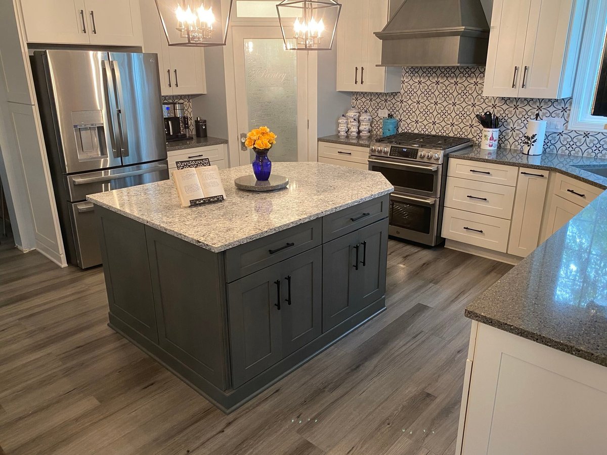 Modern kitchen with white cabinetry, dark island with granite countertop, stainless steel appliances, and wood-look flooring