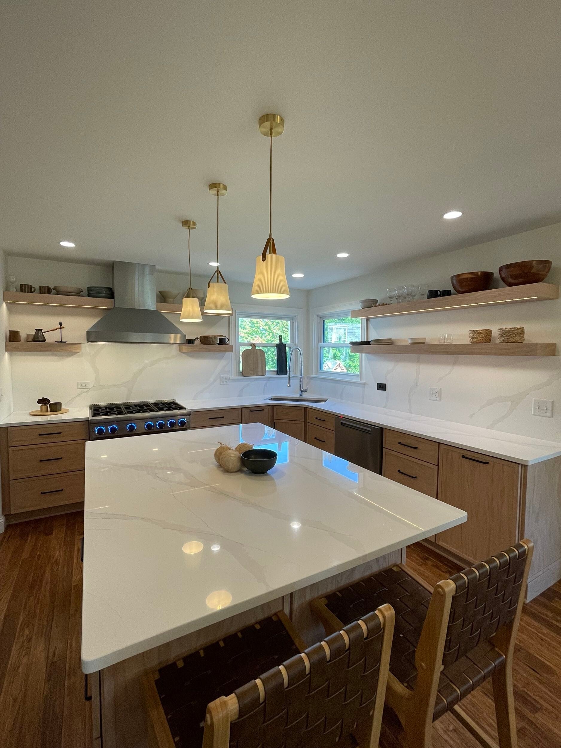 Modern kitchen with white quartz counters, wood cabinetry, pendant lights, and a center island with seating